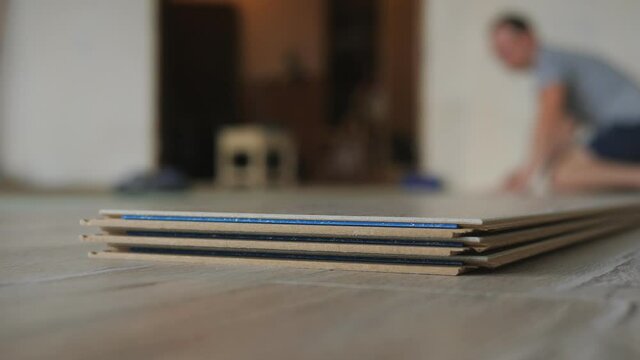 Close-up a stack of laminate is lying on the floor in the apartment, the master takes a bar of laminate and puts it on the floor.