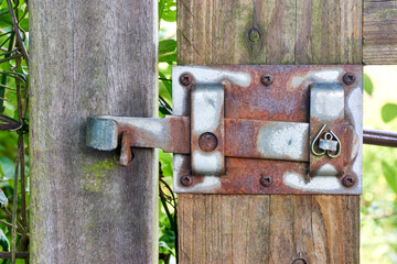 Old rusty metal gate latch on a weathered wooden garden gate in closed position.   