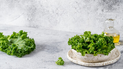Green kale leaves in white craft bowl on gray cement background. Healthy eating, vegetarian food,...