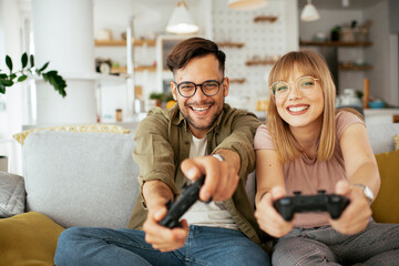 Husband and wife playing video game with joysticks in living room. Loving couple are playing video...