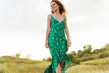 Beautiful smiling girl wearing summer dress walking in a meadow during sunset