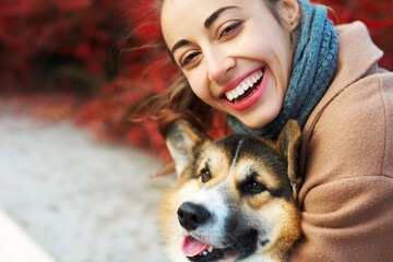 close-up autumn portrait happy woman and pet Welsh Corgi dog with funny face on red fall leaves background. spending time together outdoors at sunny autumn day