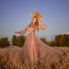 Woman in a crown of ears and a long dress among the wheat field at sunset