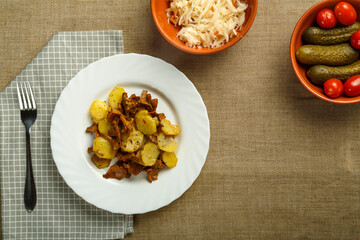 a plate of potatoes with larvae mushrooms on a napkin and a fork next to pickled cucumbers and tomatoes and cabbage.