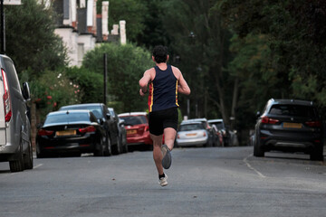 Unrecognizable runner. A man in sports outfit runs along the street. Back side.