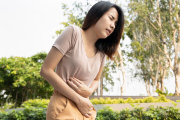 Fototapeta premium woman with stomach ache; sick asian woman suffering from stomachache, menstrual period cramp, abdominal pain, food poisoning, gastritis, acid reflux; asian young adult woman health care model