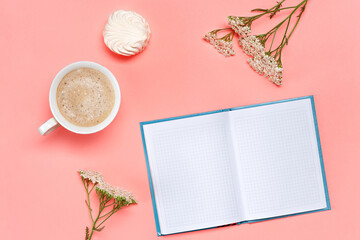 Top view of working desk with mock up blank notebook, coffee cup, marshmallow and flowers on pink background.