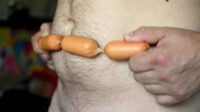 Fat belly of a man and sausages. Sausage massage. The harm of overeating. Wrong food. Obesity.