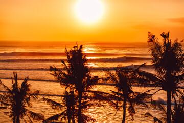 Warm sunset or sunrise with ocean wave and silhouette of tropical palms