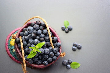 Blueberries with green leaves in a wicker basket on a gray background. Blueberry antioxidant. Healthy food and nutrition concept