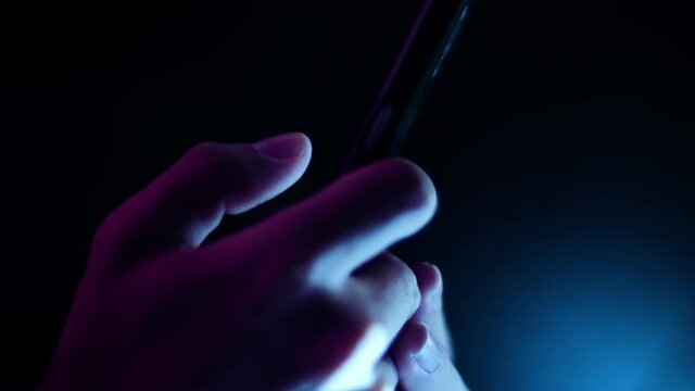 Thumb scrolling and tapping a smartphone close up side profile in a dark room with purple and blue lighting