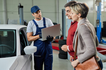 Naklejka premium Car mechanic using laptop while talking to a couple in repair shop.