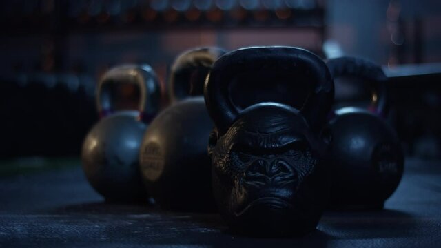 Row of Heavy Kettlebells on Gym Floor, Gorilla Face Cast Iron Weight in Low Key Lighting, Strength Training Equipment Close Up
