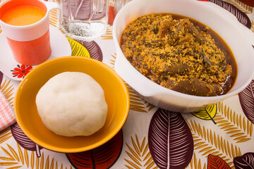 A traditional African meal of pounded yam and egusi soup in white bowl. Set on a colorful pattern...
