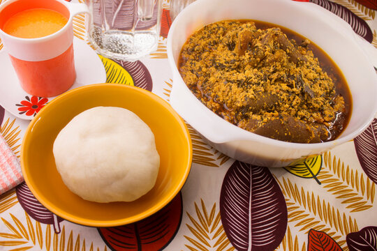 A traditional African meal of pounded yam and egusi soup in white bowl. Set on a colorful pattern table cloth