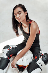 Fototapeta na wymiar Beautiful looking brunette girl with tatoos in a black tracksuit, white boots and with a motorcycle helmet, posing in a white photo studio, sitting on the floor