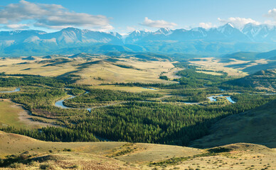 Scenic view, Altai mountains. Snow-capped peaks in blue haze, evening light. Forested river valley. 