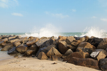 Rocky coastline with long waves lapping with sand and blue sky.
