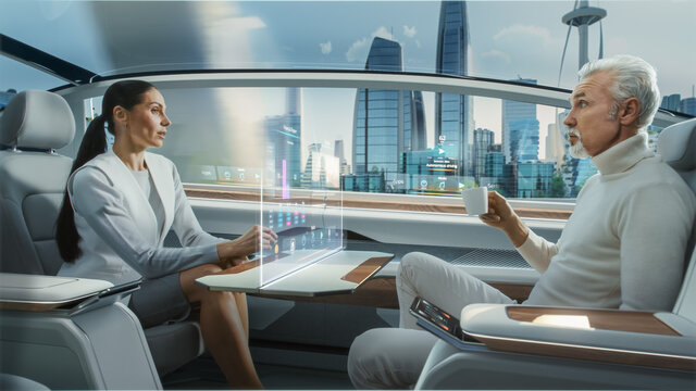 Casual Business Meeting Between Senior Male and Female inside a Futuristic Driverless Autonomous Car with Augmented Reality Presentation Interface. Self-Driving Van Driving on Downtown City Streets. 