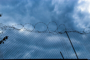 A stone fence with barbed wire at the top against a beautiful blue sky