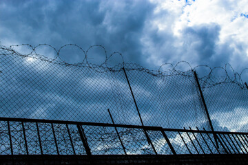 A stone fence with barbed wire at the top against a beautiful blue sky
