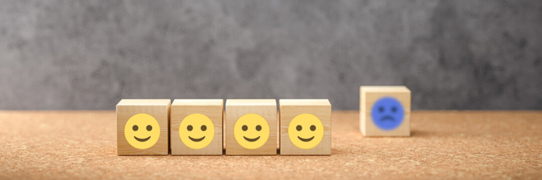 cubes with happy emoticons as a group and unhappy ones in the back on concrete background