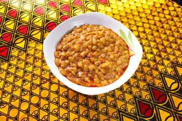 A white small bowl of porridge beans set on a colorful African pattern table cloth, Ankara.  © Afrofresh