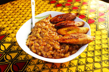 A meal of porridge beans and fried plantain with a spoon at the side. Ready to be eaten. 
