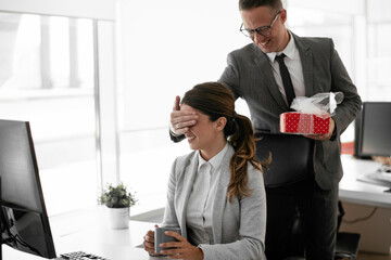 Young businessman giving his colleague present in office. Young man suprise beautiful businesswoman in office.