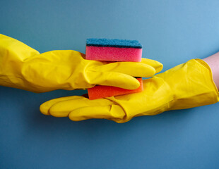 yellow gloves hold dishwashing sponge on blue background