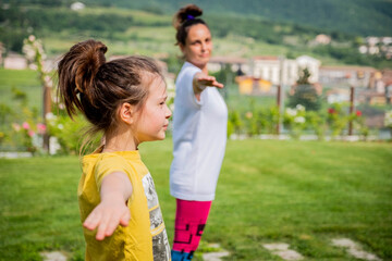 Fototapeta premium Mother and daughter doing yoga exercises outdoor - young woman doing fitness exercises in the park - Reach harmony