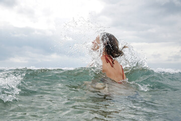 Back view of a young woman in the ocean enjoying cool ocean water during vacation. Freedom and happiness concept. 
