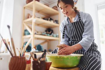 Young female ceramist working by using pottery wheel indoors and making handmade clay product