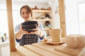 Job is done. Young female ceramist indoors with finished handmade clay product. Conception of pottery