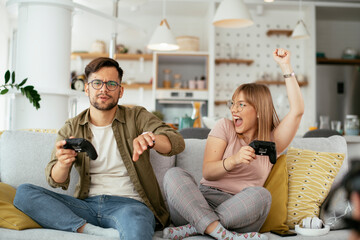 Husband and wife playing video game with joysticks in living room. Loving couple are playing video games at home.. © JustLife