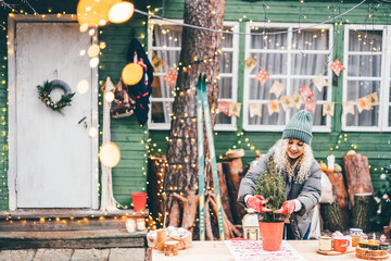 Woman decorating home for Christmas and holding small Christmas tree outside.