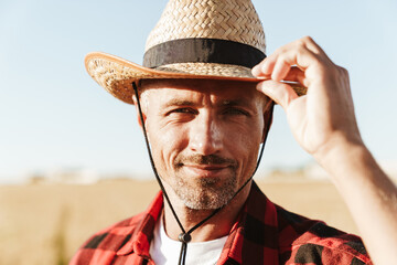 Fototapeta premium Image of pleased man looking at camera while standing at cereal field