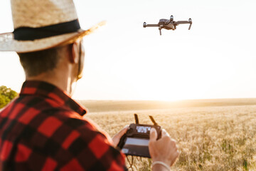 Image from back of man using drone while standing at cereal field