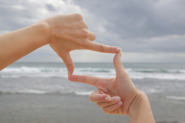 Woman holds hands in the shape of a frame in front of blue ocean horizon
