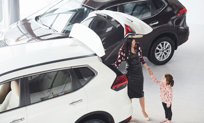 Mother with her daughter walking together near modern automobile indoors