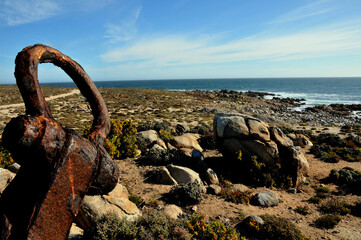 A red rusty anchor as part of an endless and rugged West Coast vista