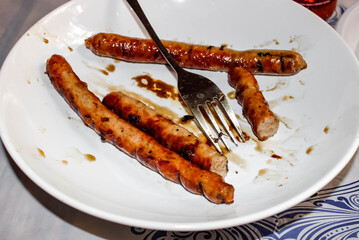 Half-eaten barbecue sausages from the grill lie with a fork on a plate.
