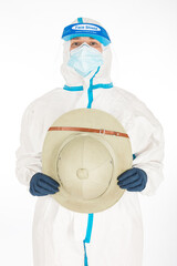 Fototapeta premium Woman doctor wearing PPE to fight the coronavirus, holding in her hands a colonial-era explorer's hat, on white background. Warrior. COVID medicine concept