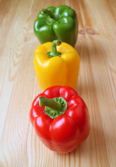 Vibrant Tricolor Bell Peppers Lined Up on Light Brown Wooden Background