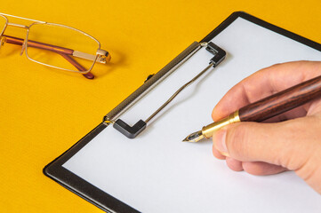 The hand holds stylish pen for writing text on a blank sheet of paper