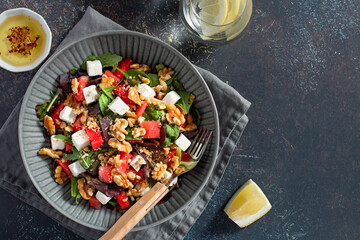 Summer refreshing salad with watermelon, feta cheese, walnuts and greens on black table top with lemon water, top view. Recipe for heat wave