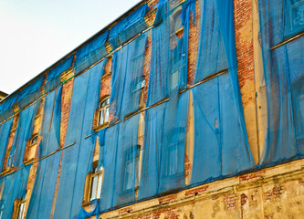The facade of an old ruinous building is mantled with some blue curtains to protect the pedestrians