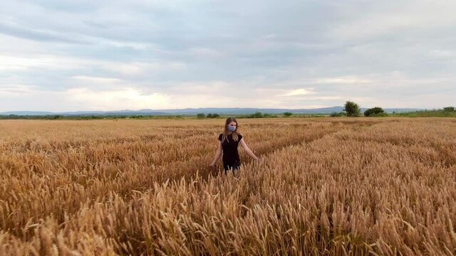 Girl in a mask against the virus, walking in a beautiful field of wheat