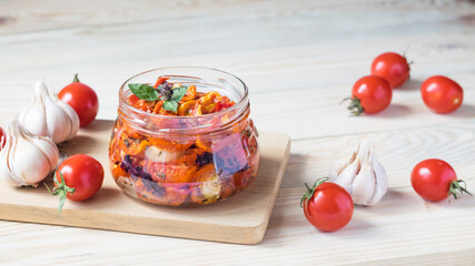 Sun dried tomatoes in glass jar with ripe tomatoes and garlic on cutting board, on wooden background