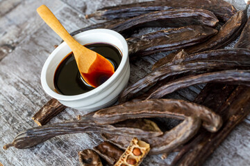 Carob molasses and carob pods on wooden background